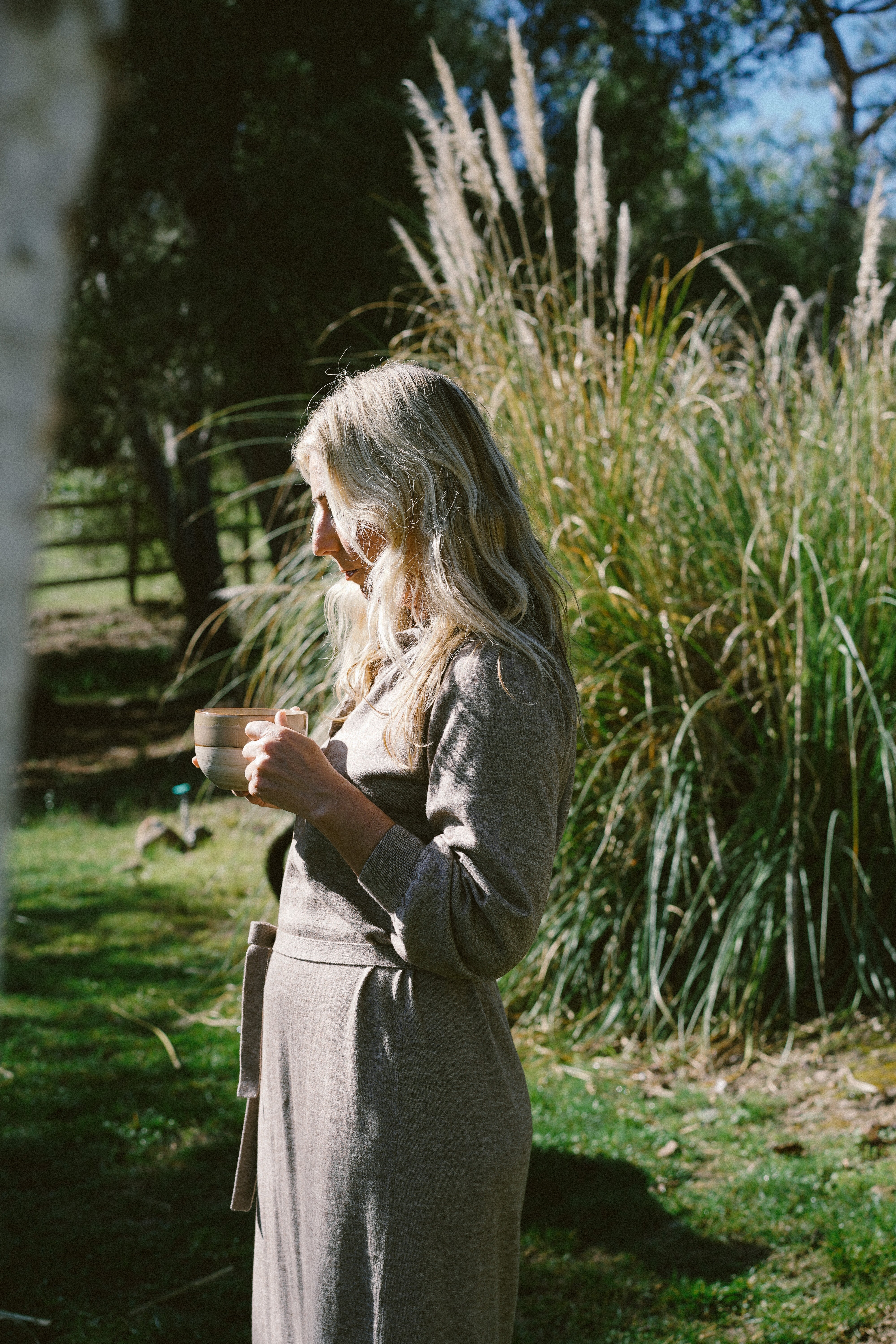 Woman in linen dress holding a tea bowl in nature, cyclical wellness ritual