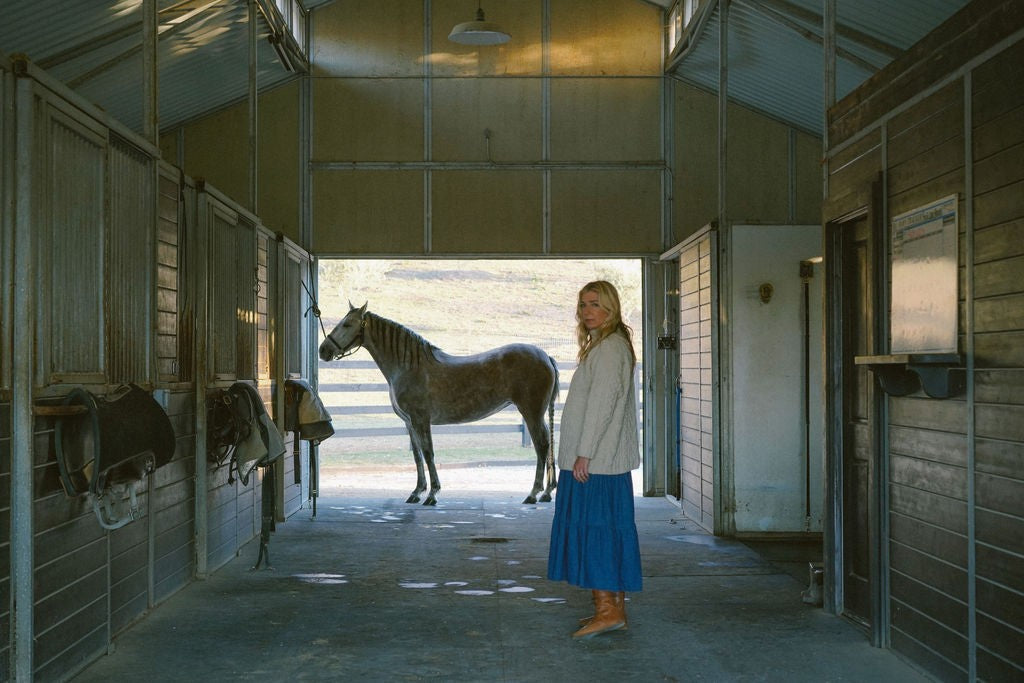Woman standing in horse stable with grey horse, Feral Future The Return course