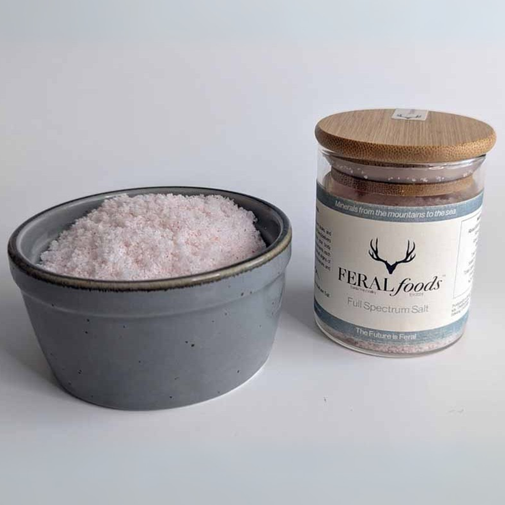Jar of Feral Foods full spectrum salt next to a bowl of pink salt on a white background